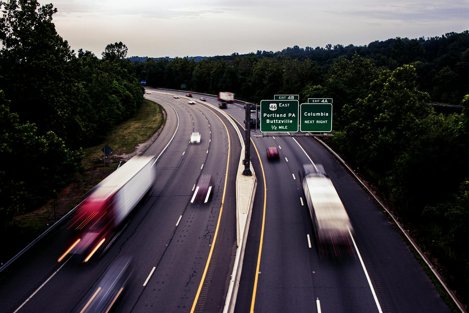 fast moving cars on an expressway between green trees